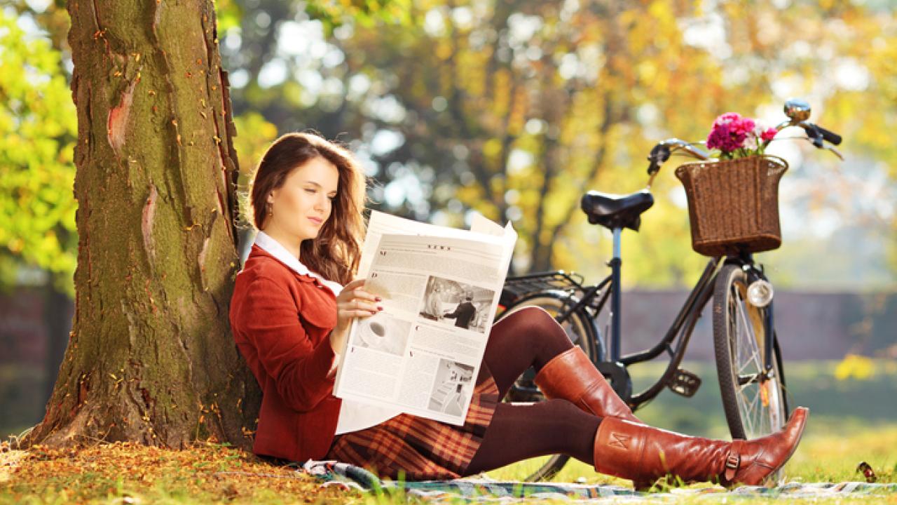 Woman reading the paper outside with her bike.